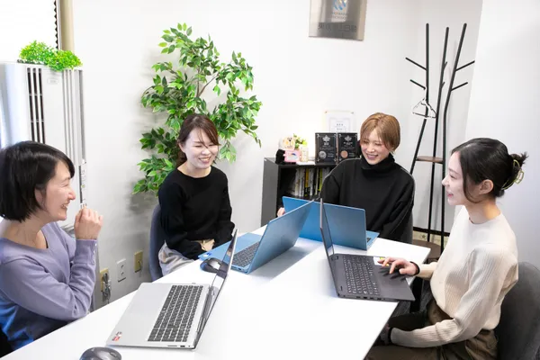 4名の女性がノートパソコンを開きながら机を囲んで談笑している