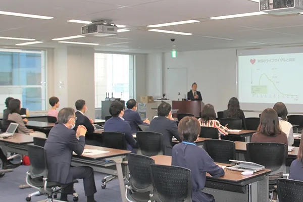 セミナー会場写真。スライドが投影され、参加者は長机に座っている