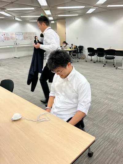 生理痛を疑似体験する装置を装着した男性が椅子に座り、痛みに顔をしかめている様子。