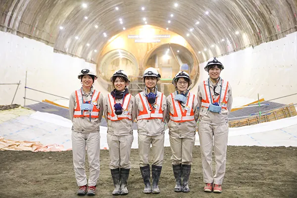 工事中のトンネルを背景にした作業服を着ている5名の女性の写真